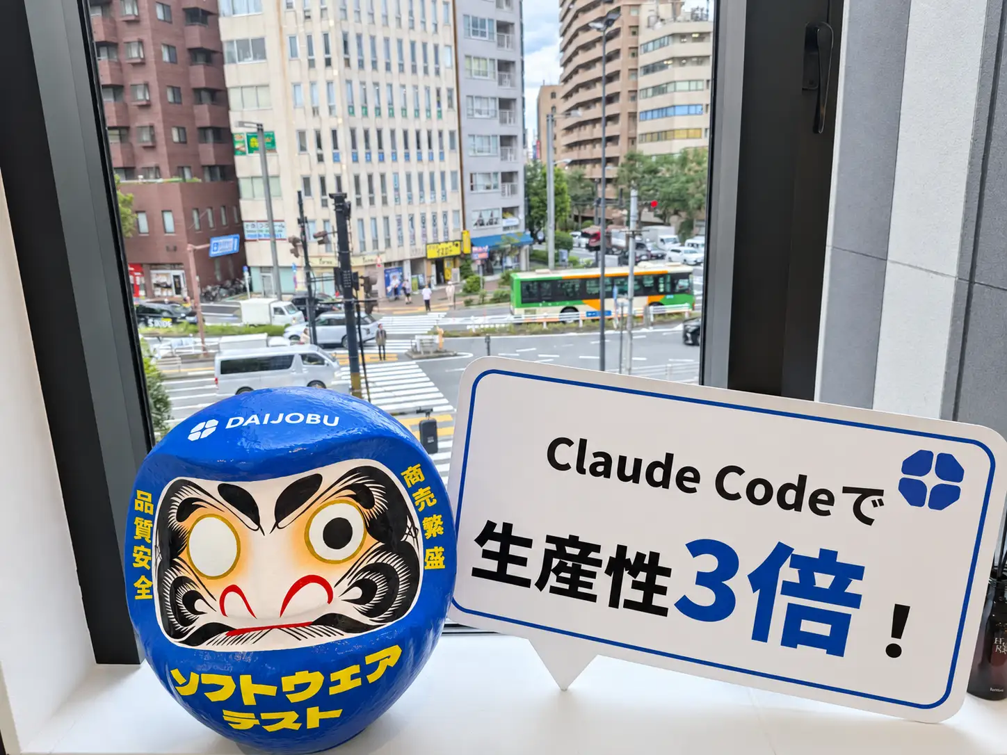 DAIJOBUオフィスの青いだるまと「Claude Codeで生産性3倍！」の看板